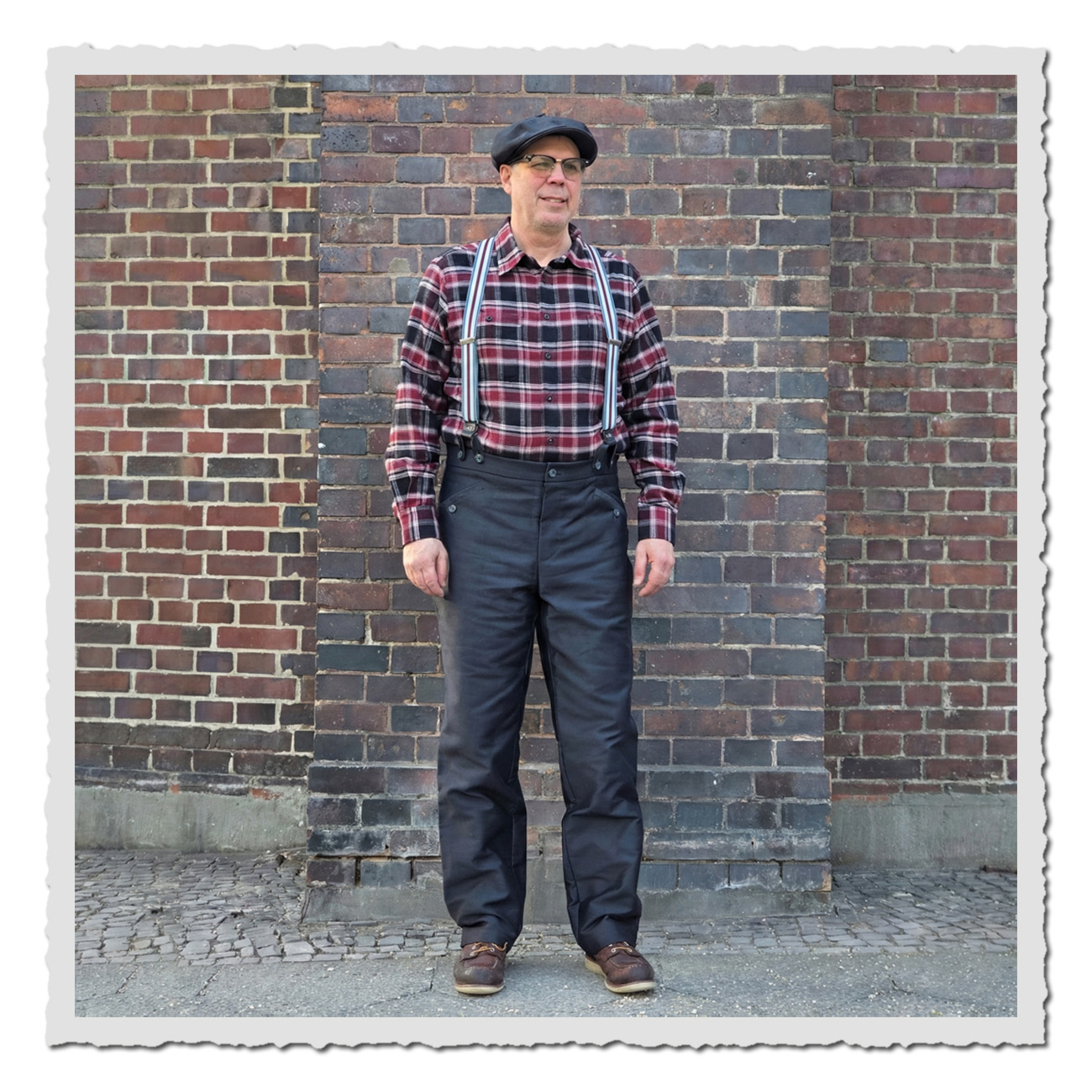 Mann in Arbeiterhose Gustav I in Anthrazit, hohe Leibhöhe und Cinch-Back, getragen im Vintage-Workwear-Look vor Ziegelwand.